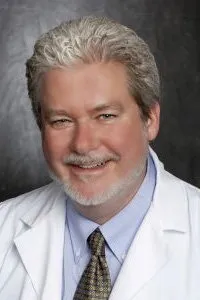 A man with grey hair and white shirt smiling.